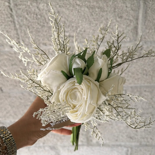 Bouquet of white roses and greenery held by a hand against a neutral background