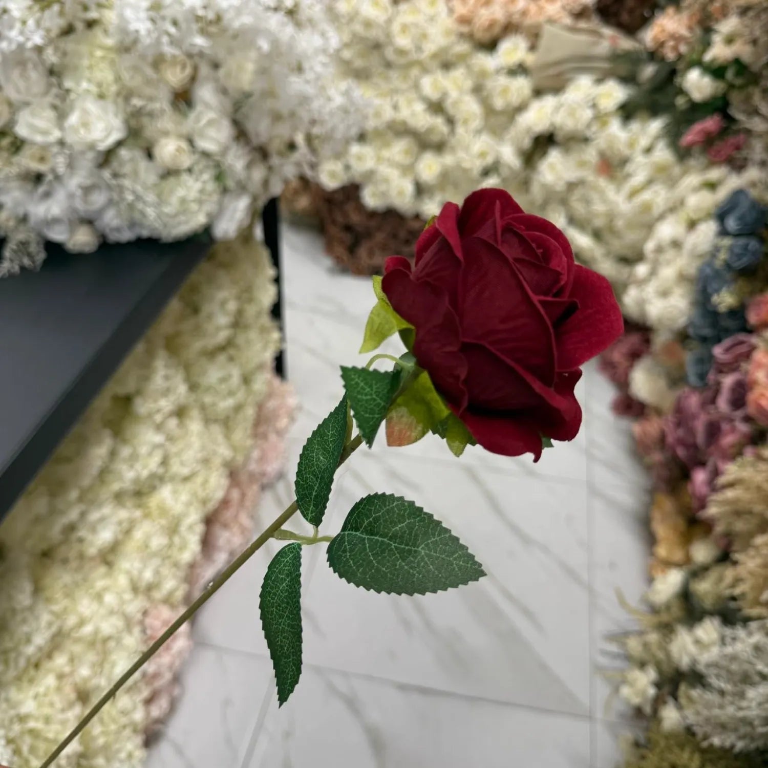 Single red rose with green leaves against a blurred floral background