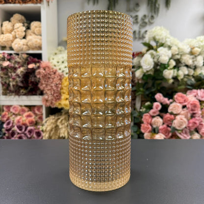 amber beaded vase on a dark surface with floral arrangements in the background