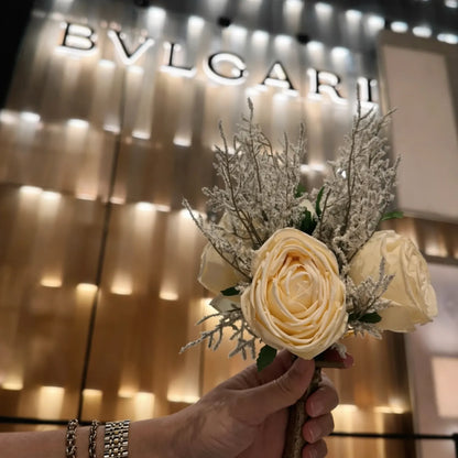 Hand holding a bouquet of flowers in front of a BVLGARI store sign.
