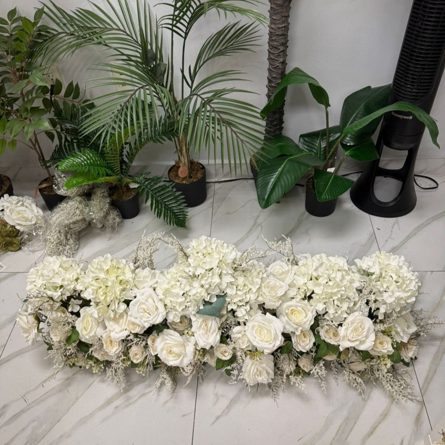 Floral arrangement on a marble floor with plants in the background