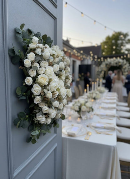 Decorative floral arrangement on a door with a wedding reception setup in the background.