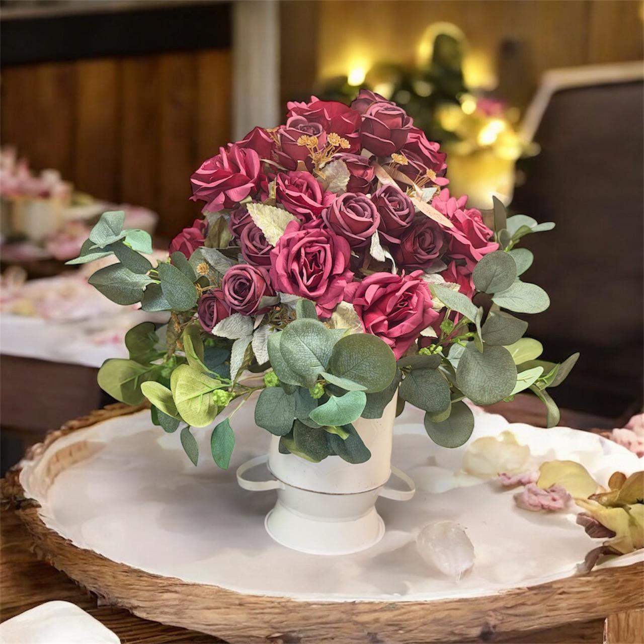 Bouquet of pink and red roses with greenery on a wooden table.
