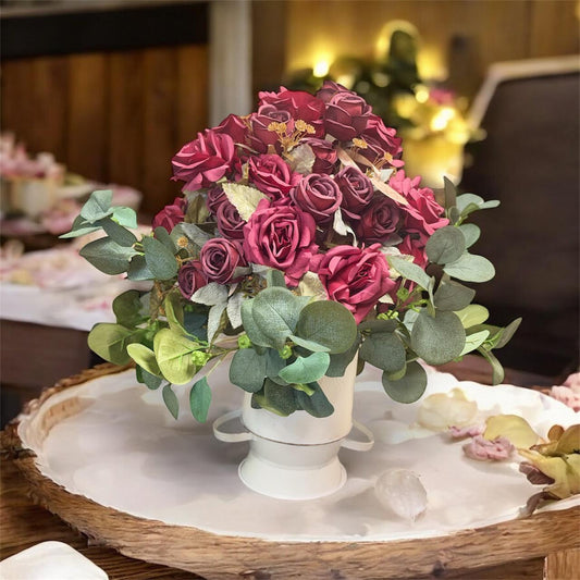 Bouquet of pink and red roses with greenery on a wooden table.
