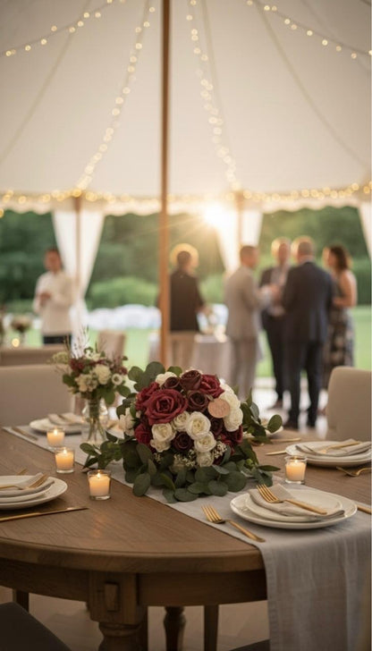 Decorative floral arrangement on a table with people in the background under a tent.