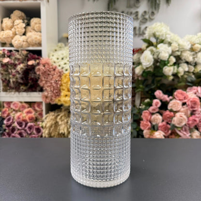 Decorative crystal vase on a dark surface with floral arrangements in the background.