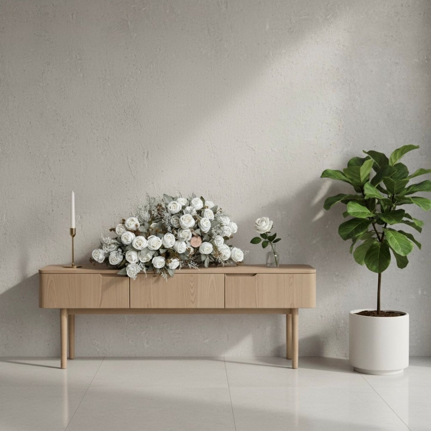 Wooden console table with flowers and a candle next to a potted plant against a gray wall.