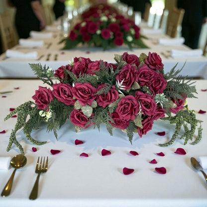Decorative table setting with red roses and greenery on a white tablecloth.