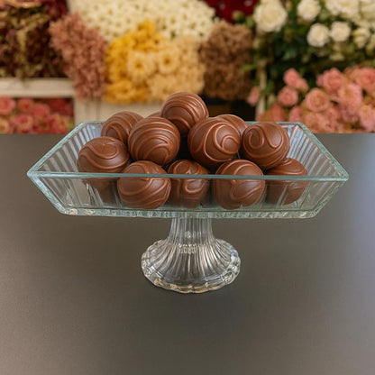 Glass dish with chocolate truffles on a table with floral decorations in the background