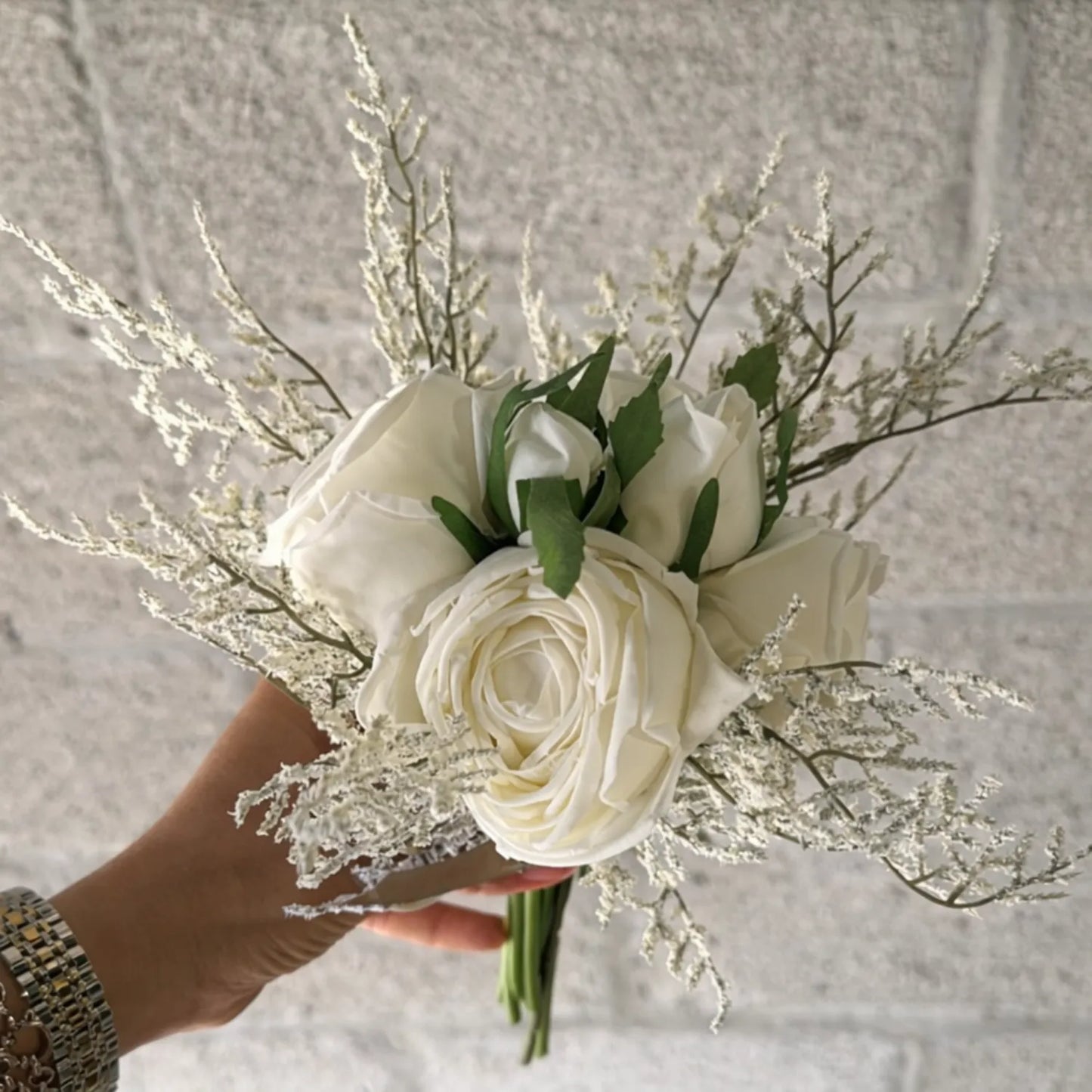 Bouquet of white roses and greenery held by a hand against a neutral background