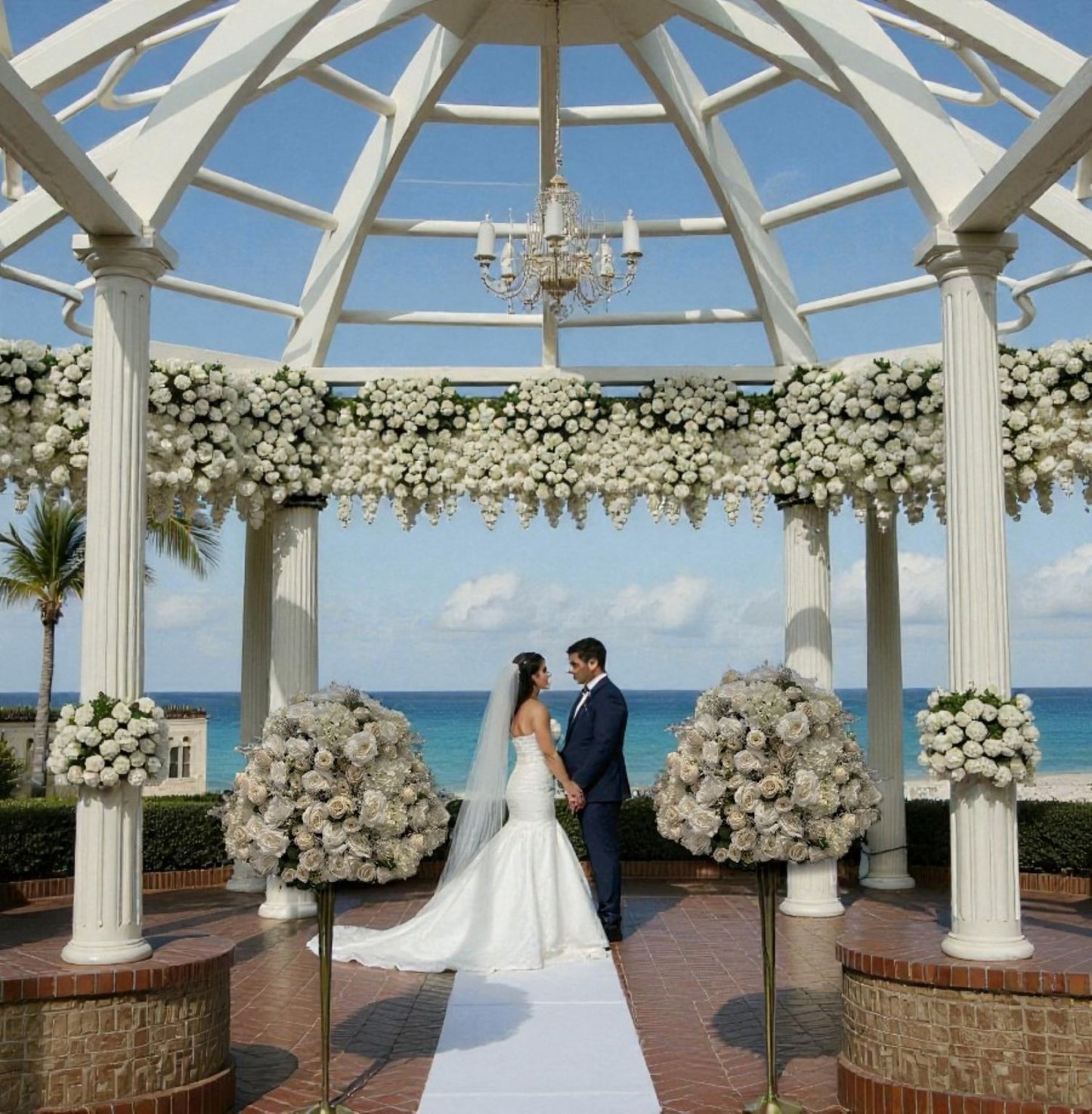 Wedding couple standing under a decorated gazebo with floral arrangements by the ocean.