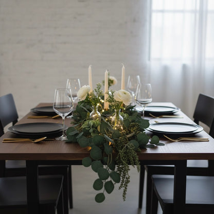 Dining table set with black plates, glasses, and a floral centerpiece.