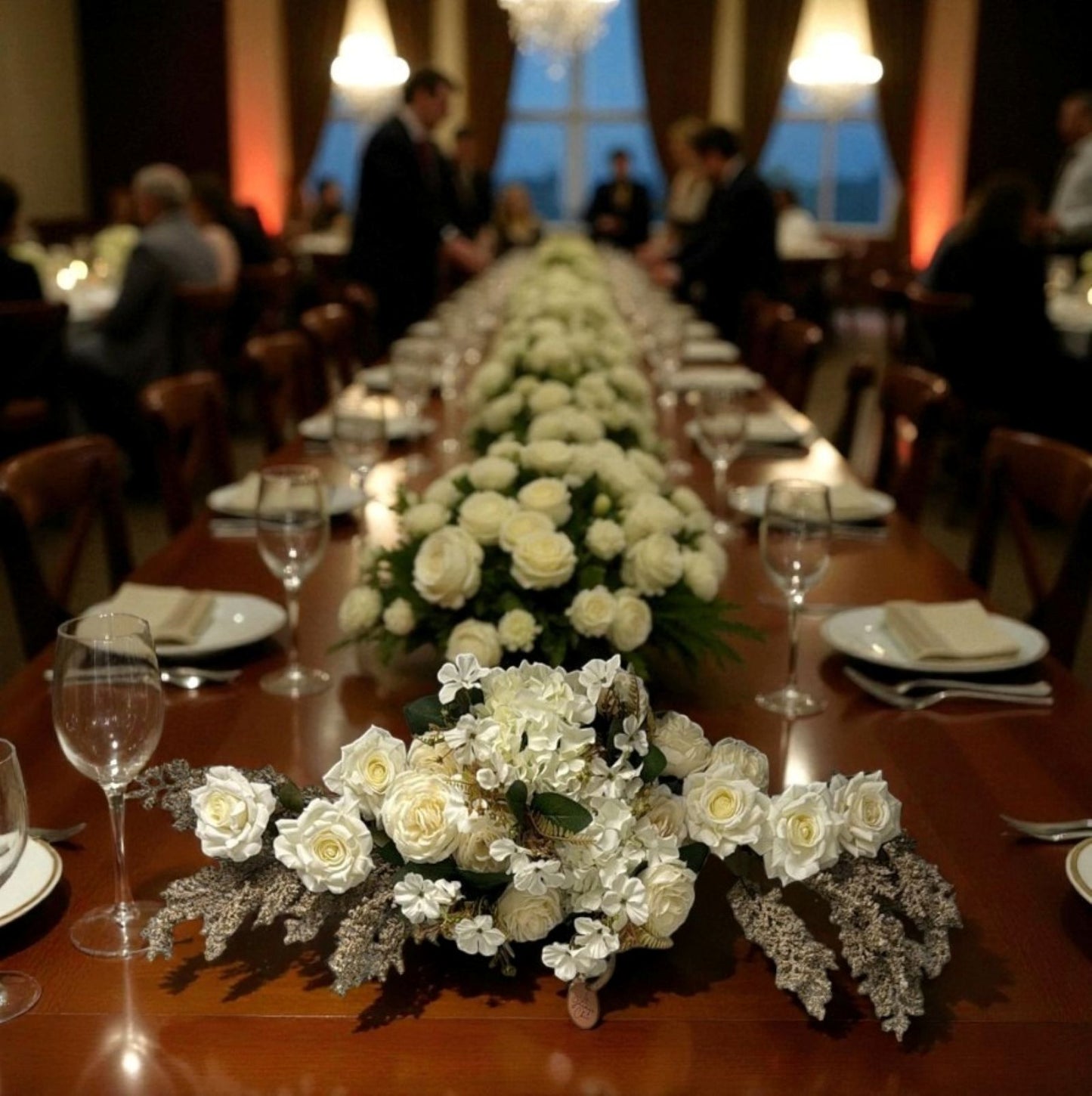 Long dining table set with white floral arrangements, glasses, and silverware in a formal setting.
