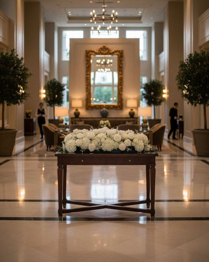 Luxurious hotel lobby with a table of white flowers and decorative mirror.