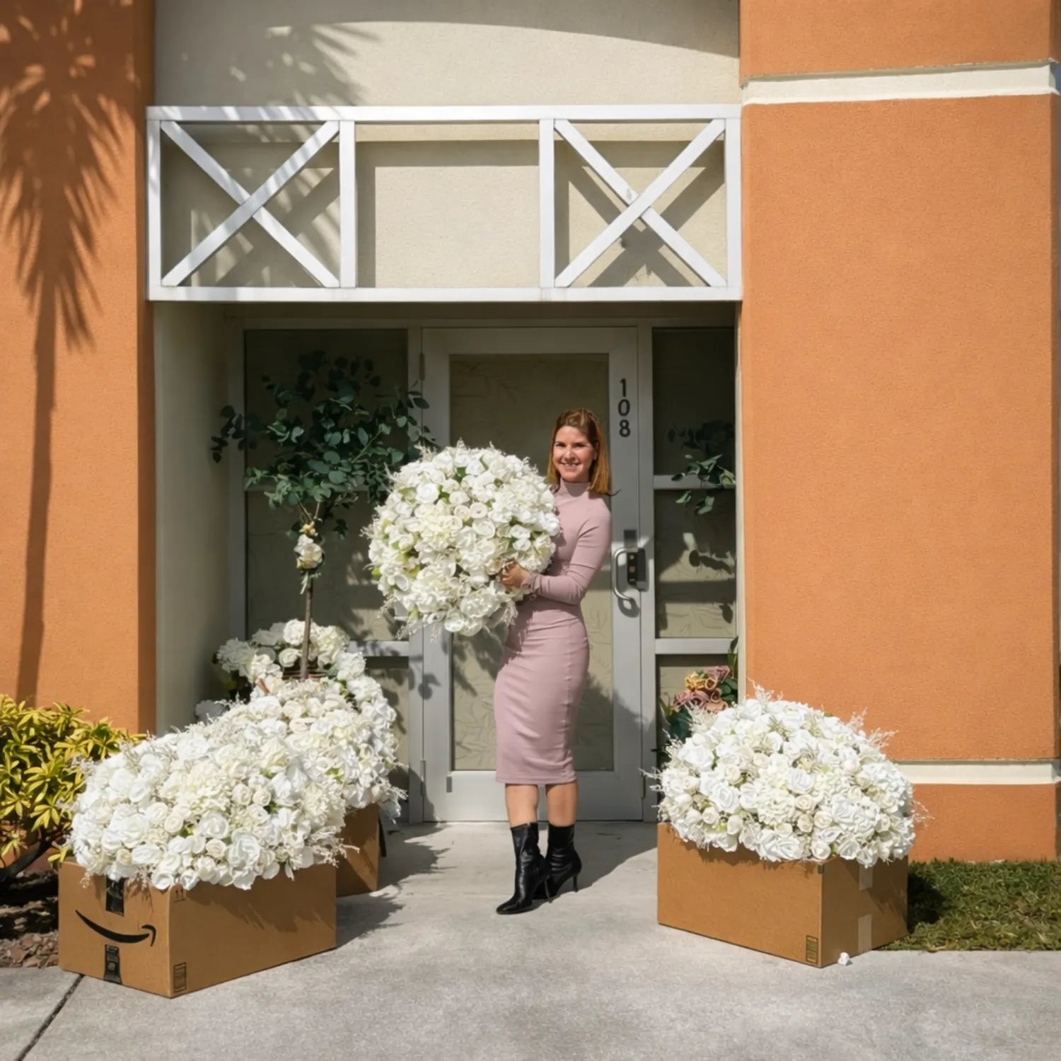 Woman holding a large bouquet of white flowers in front of a building with flower arrangements on either side.