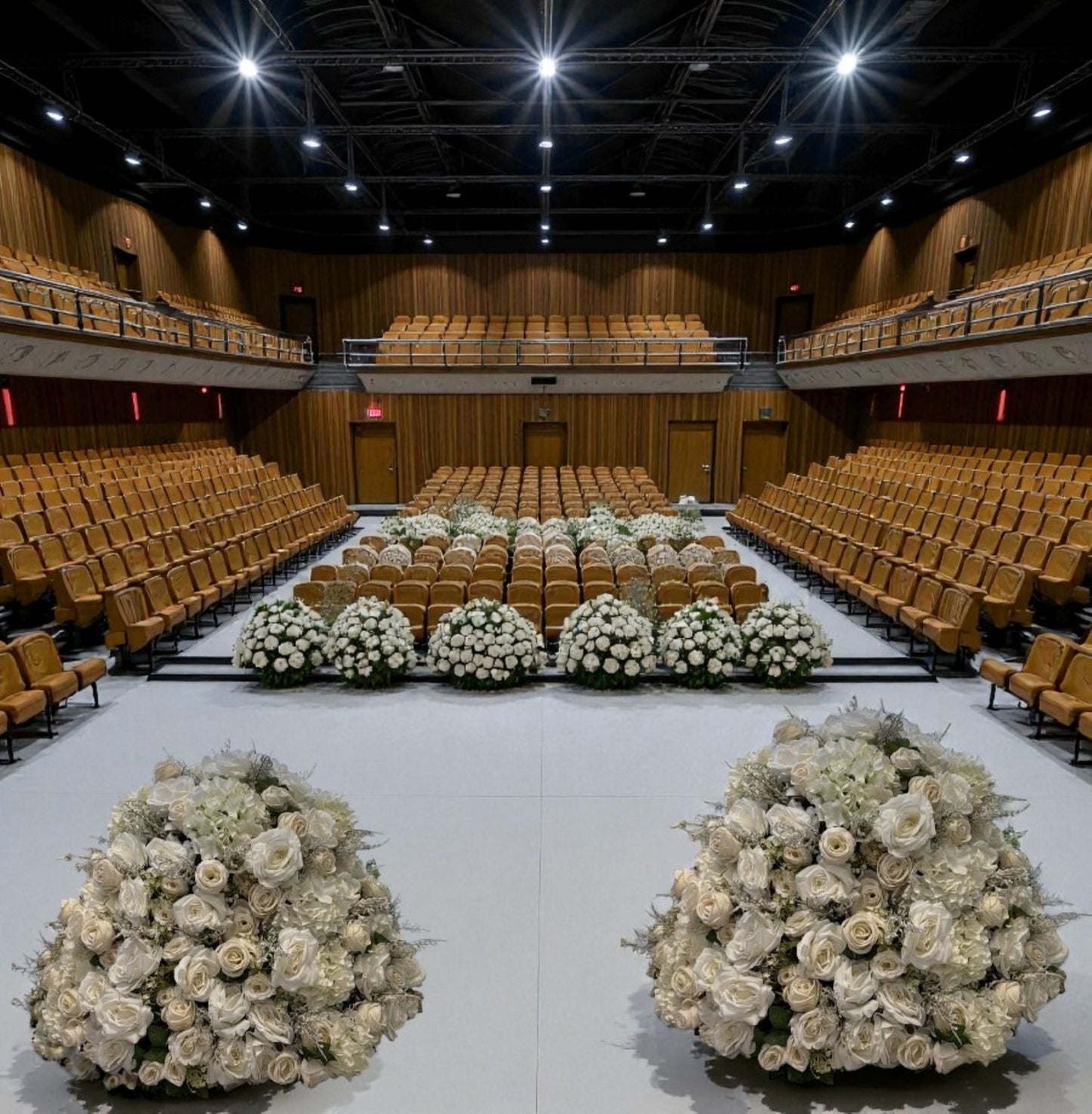 Large auditorium with rows of chairs and decorative flower arrangements on the floor.