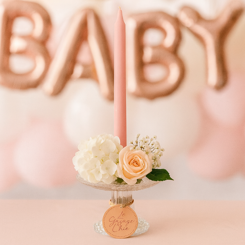Pink candle with flowers on a stand in front of rose gold 'BABY' balloons.