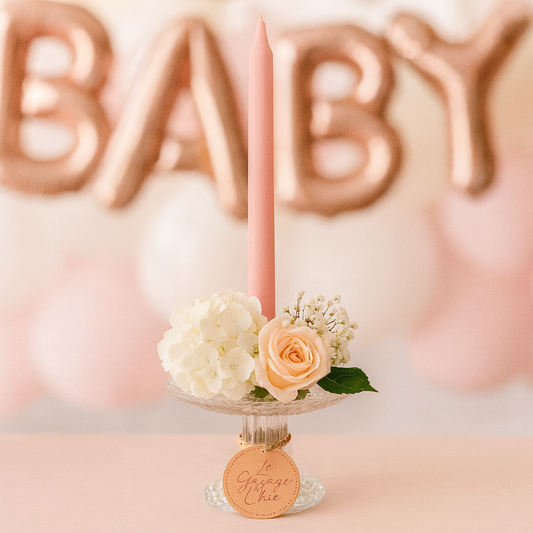 Pink candle with flowers on a stand in front of rose gold 'BABY' balloons.