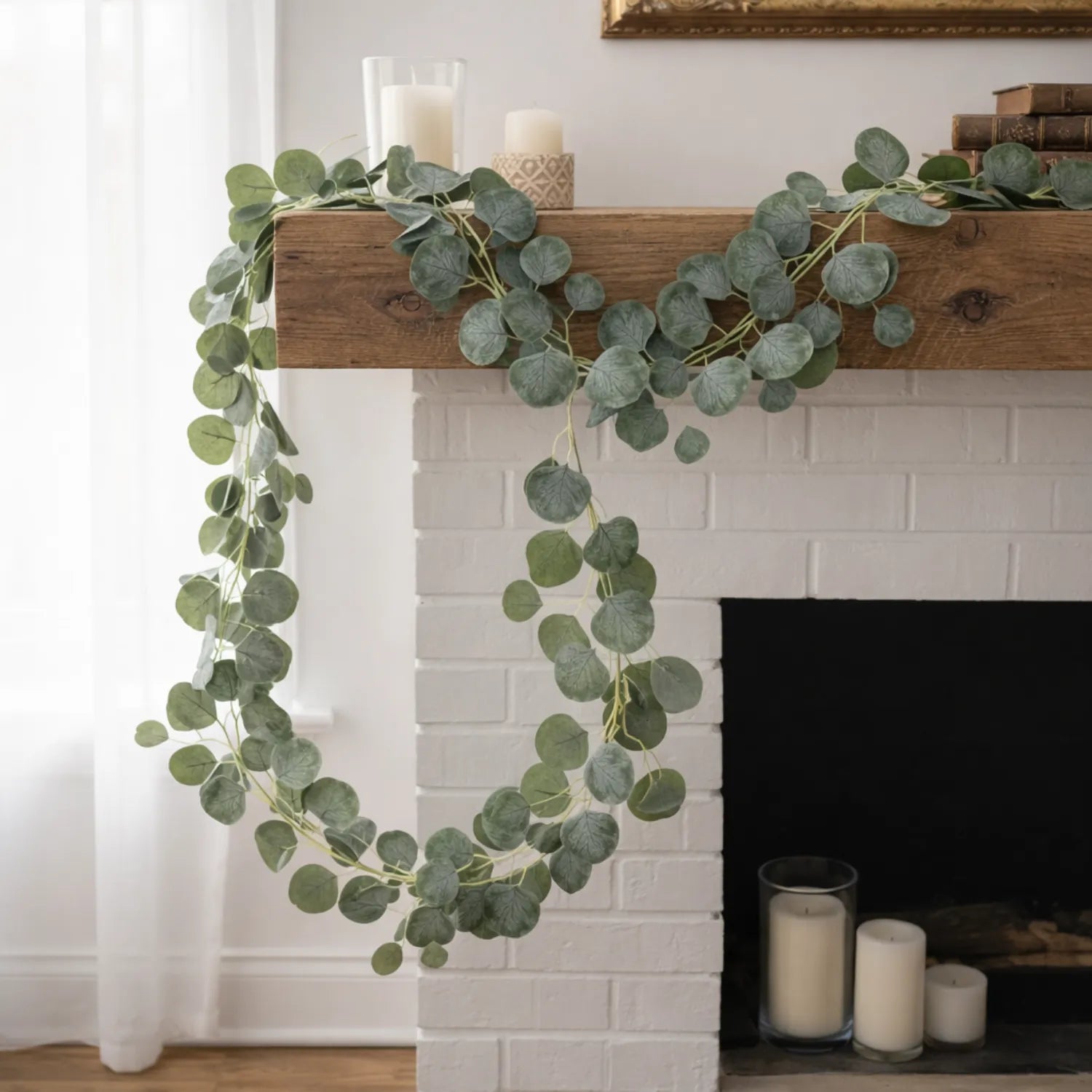 Green leafy garland draped over a wooden mantel with candles on a fireplace.