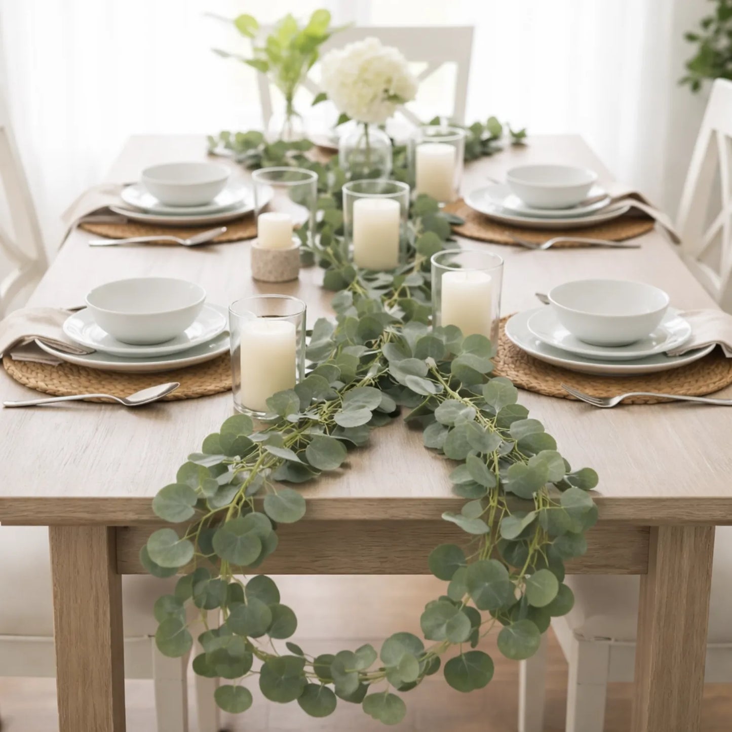 Elegant table setting with greenery and candles on a wooden table.