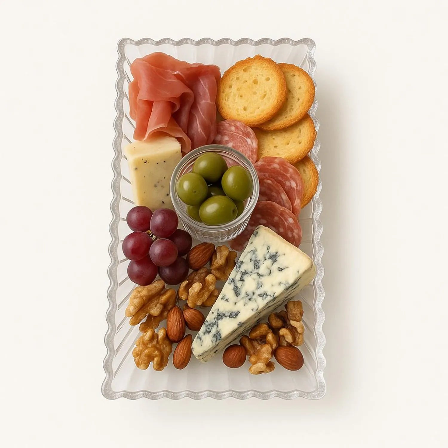 Assorted meats, cheeses, fruits, and nuts on a decorative platter with a white background