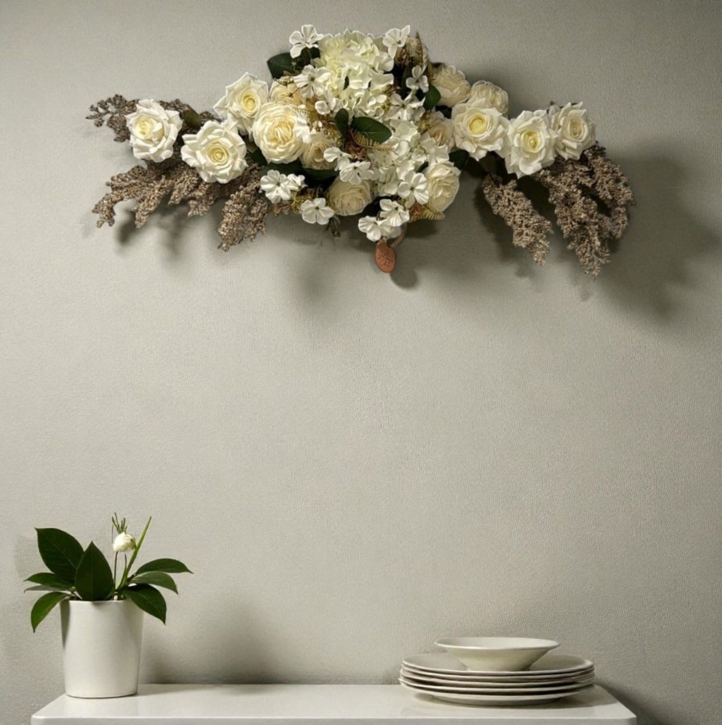 Floral arrangement on a wall above a table with plates and a plant.