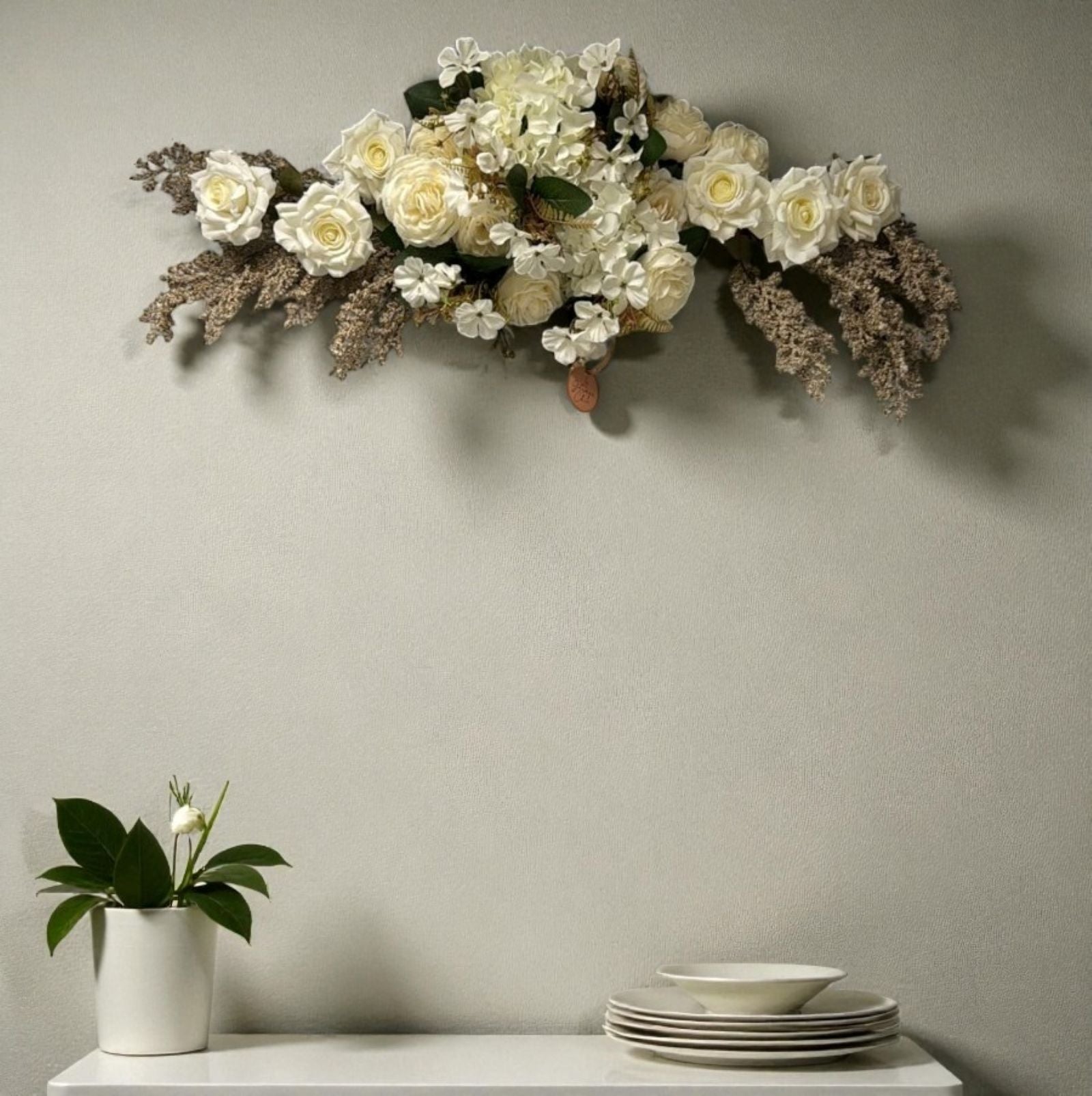 Floral arrangement on a wall above a table with plates and a plant.