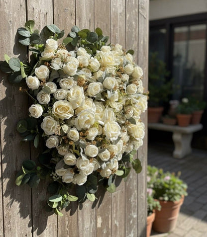 Floral wreath with white flowers and green leaves attached to a wooden door.