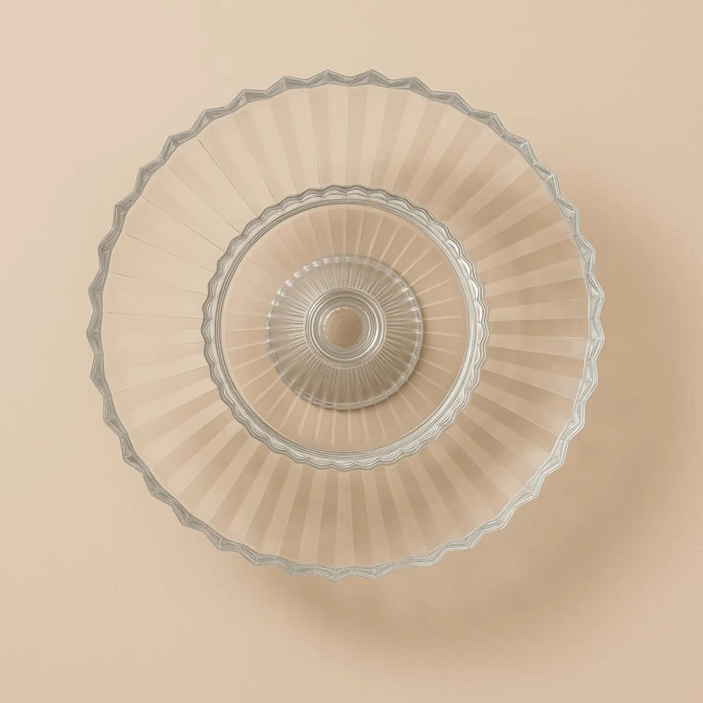 Clear glass cake stand with decorative rim on a beige background