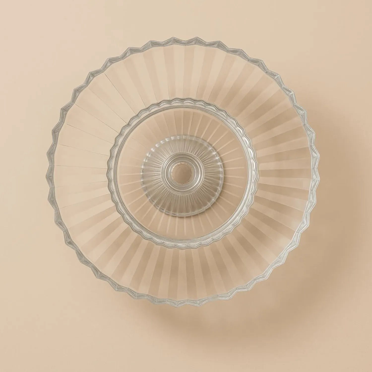 Clear glass cake stand with decorative rim on a beige background