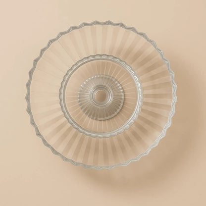 Clear glass cake stand with decorative rim on a beige background