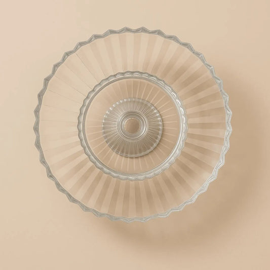 Clear glass cake stand with decorative rim on a beige background