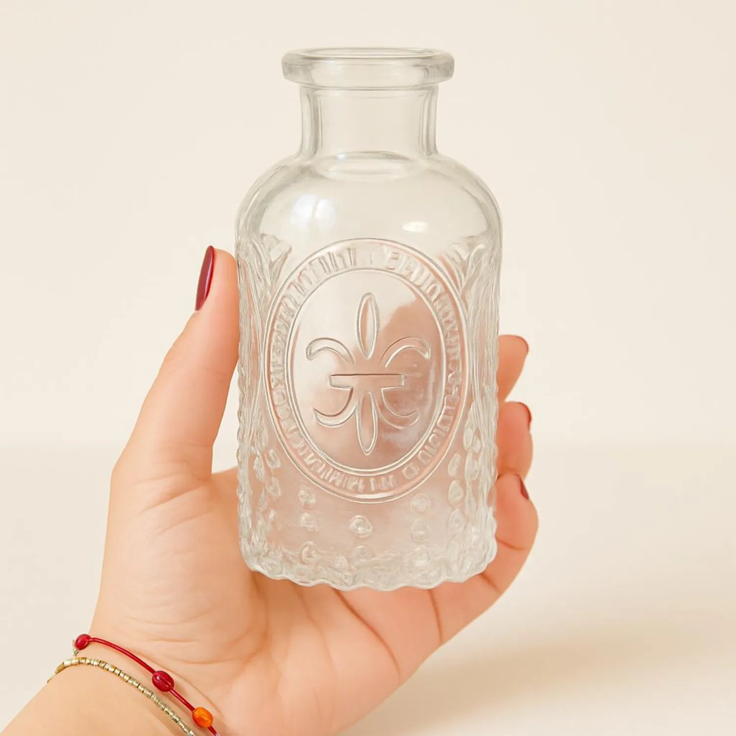 Hand holding a small glass bottle with embossed design against a plain background