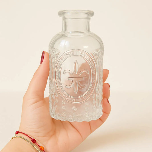 Hand holding a small glass bottle with embossed design against a plain background