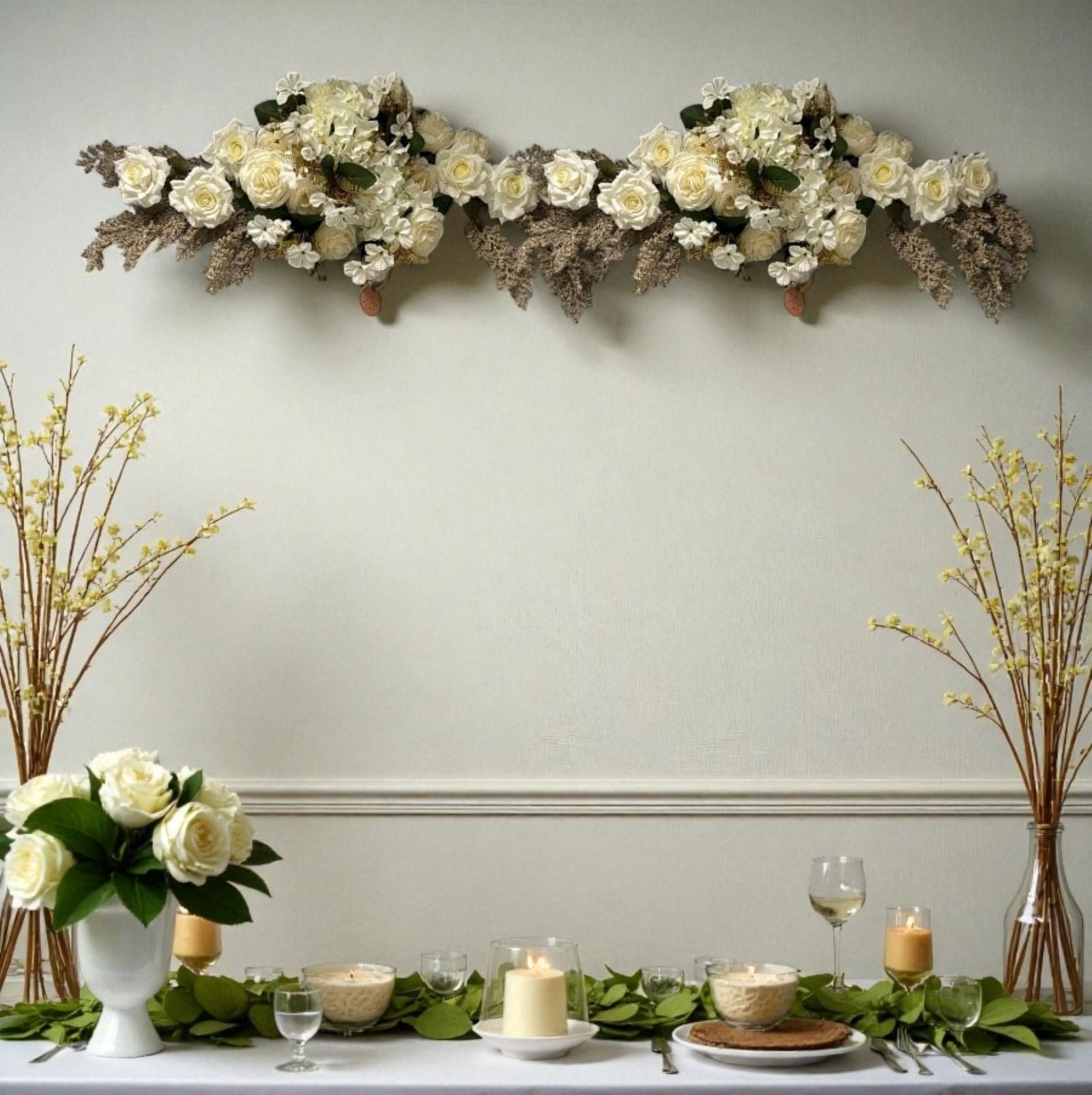 Decorative floral arrangement on a wall above a table set with candles and glasses.