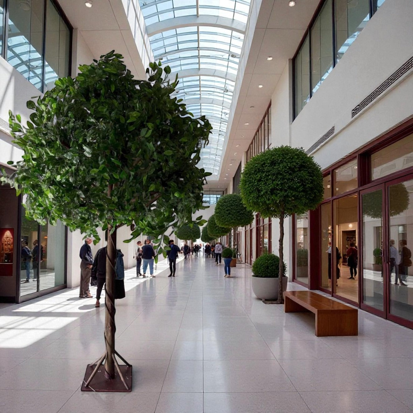 Modern indoor atrium with people walking, large trees, and glass ceiling
