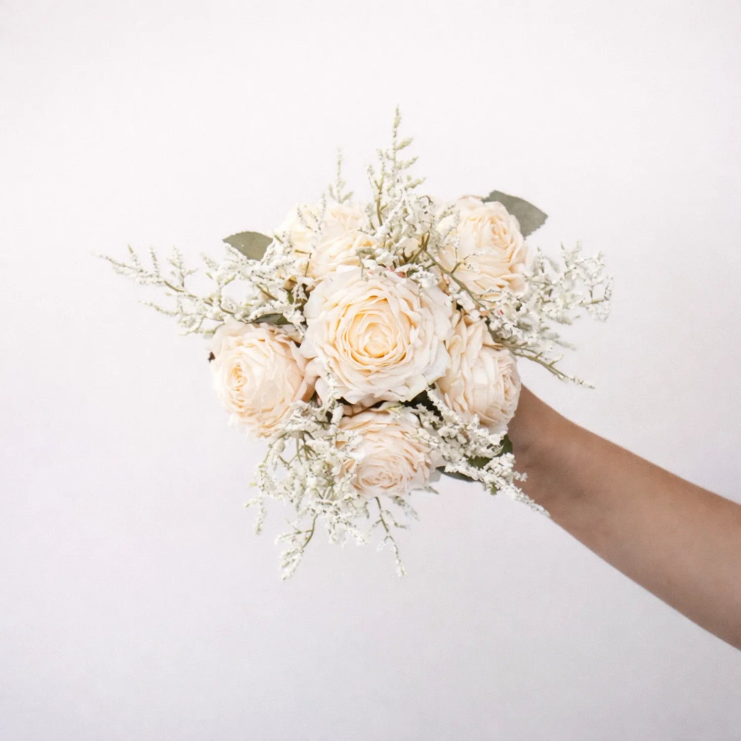 Bouquet of white roses held by a hand on a light background