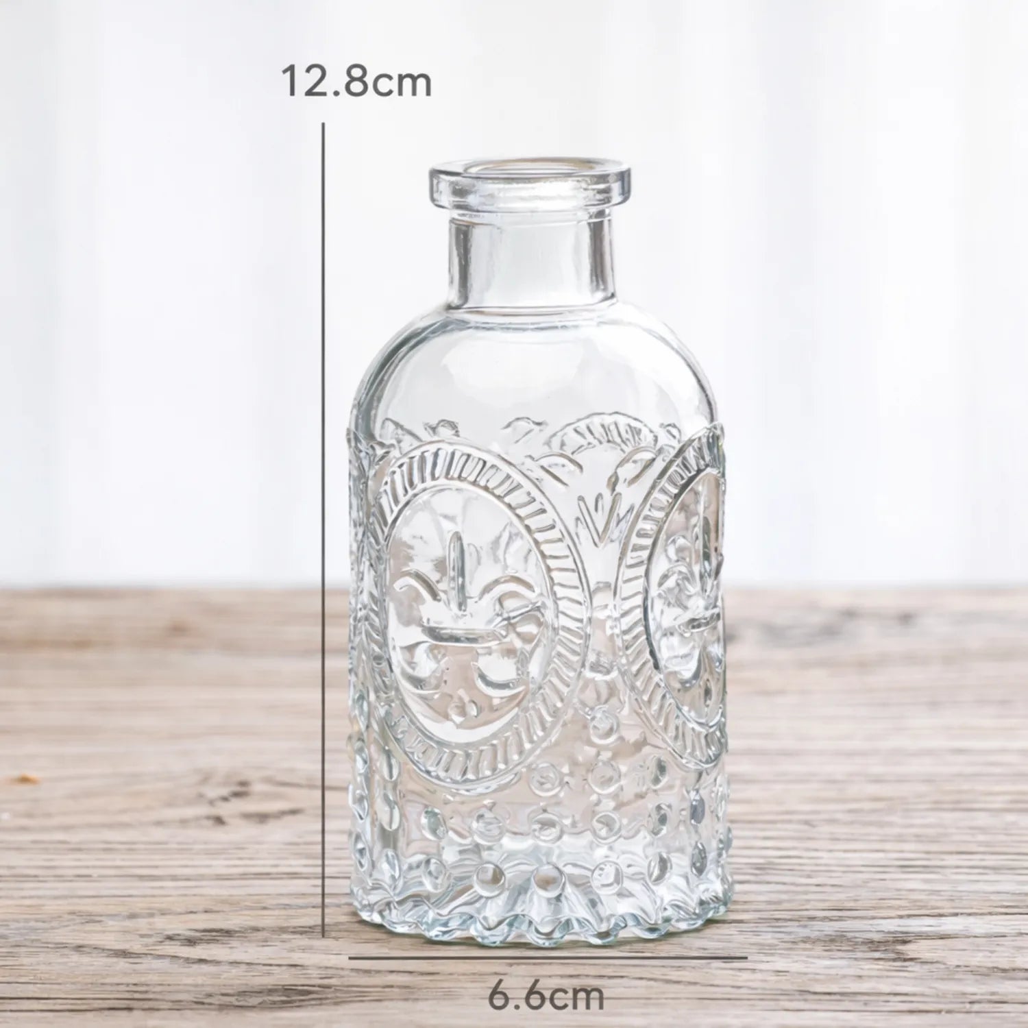 Decorative glass bottle with embossed design on a wooden surface, shown with measurements.
