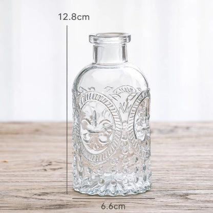 Decorative glass bottle with embossed design on a wooden surface, shown with measurements.