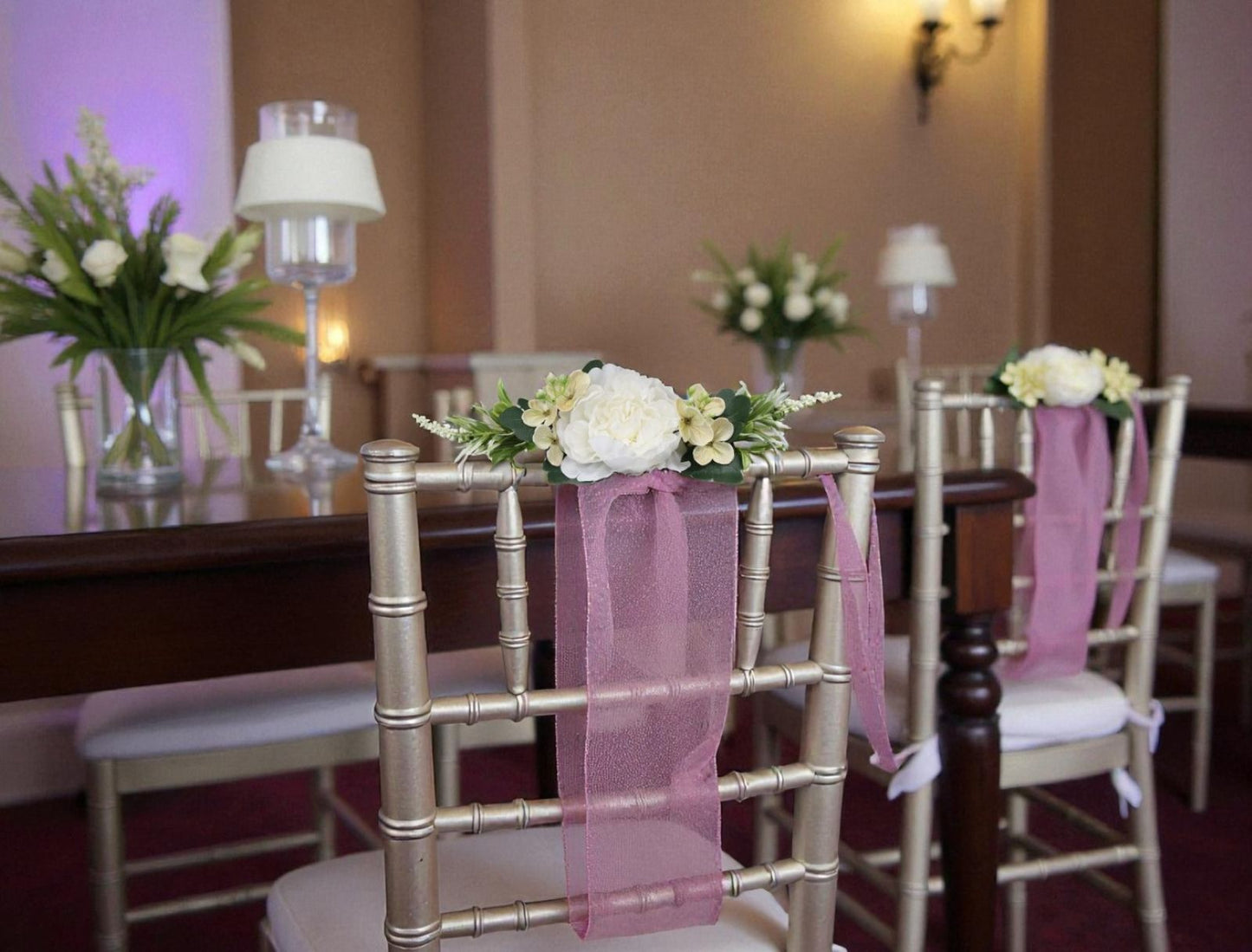Decorated chairs with pink ribbons and floral arrangements in a formal setting.